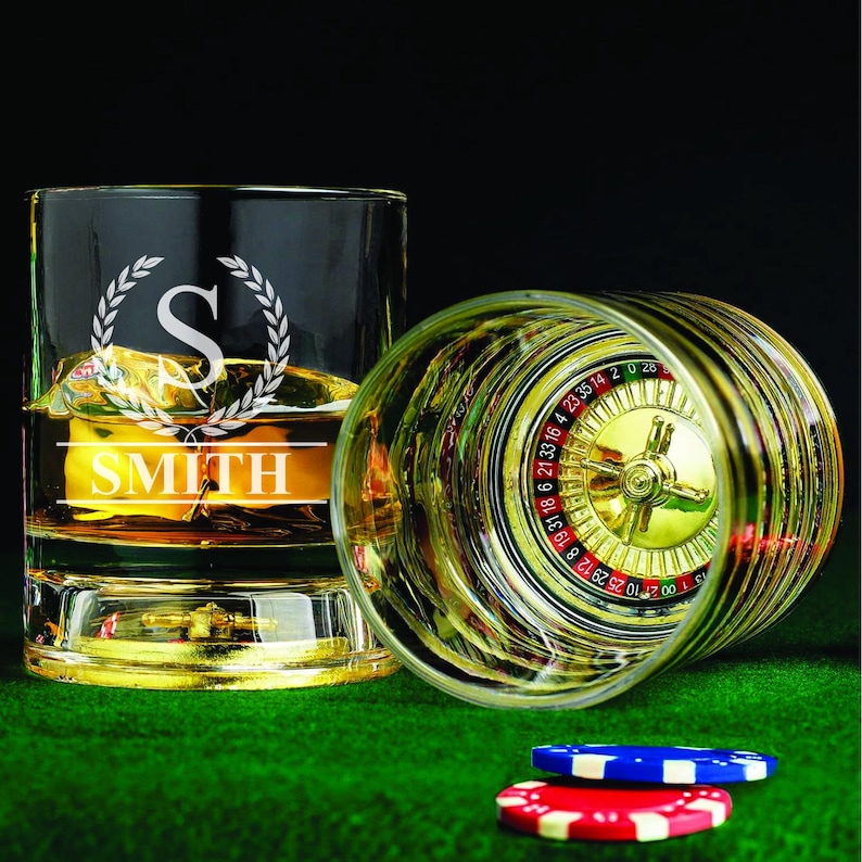 May include: Two clear glass tumblers with a gold rim. One tumbler has a roulette wheel design and the other has a personalized design with the letter "S" and the name "SMITH".