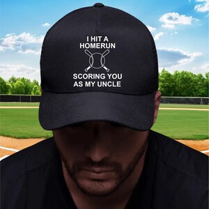 May include: Black baseball cap with white text that reads "I HIT A HOMERUN SCORING YOU AS MY UNCLE" with a baseball and crossed bats graphic. The cap has a mesh back.