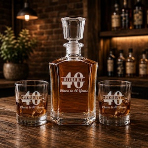 May include: A personalized whiskey decanter set with two glasses. The decanter and glasses are engraved with "ROBERT", the number "40", and "Cheers to 40 Years". The set is filled with amber liquid and sits on a wooden surface.
