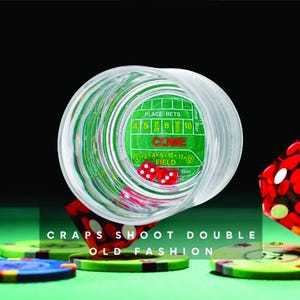 May include: A clear glass shot glass with a green felt casino craps layout inside. The glass is tipped over, revealing two red dice. The glass is surrounded by colorful casino chips.