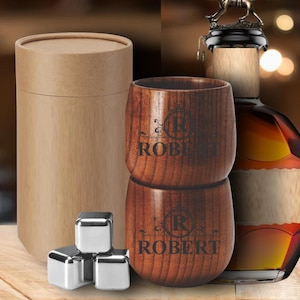 May include: A wooden tumbler set with the name "ROBERT" engraved on each cup. The set includes stainless steel ice cubes and a cylindrical cardboard container. A bottle of liquor is visible in the background.