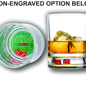 May include: A clear glass with a green and white dice game design on the bottom. The glass is filled with a golden liquid and ice cubes. Two red dice are visible at the bottom of the glass.
