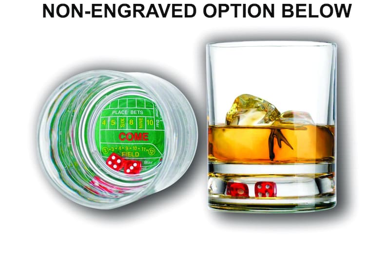 May include: A clear glass with a green and white dice game design on the bottom. The glass is filled with a golden liquid and ice cubes. Two red dice are visible at the bottom of the glass.