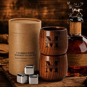 May include: A whiskey glass set with two wooden glasses engraved with "MIGUEL" and the letter "M". The set includes a bottle with a deer-shaped stopper, whiskey stones, and a cylindrical box that reads "CHARRED WOOD WHISKEY GLASS SET WITH WHISKEY STONES."