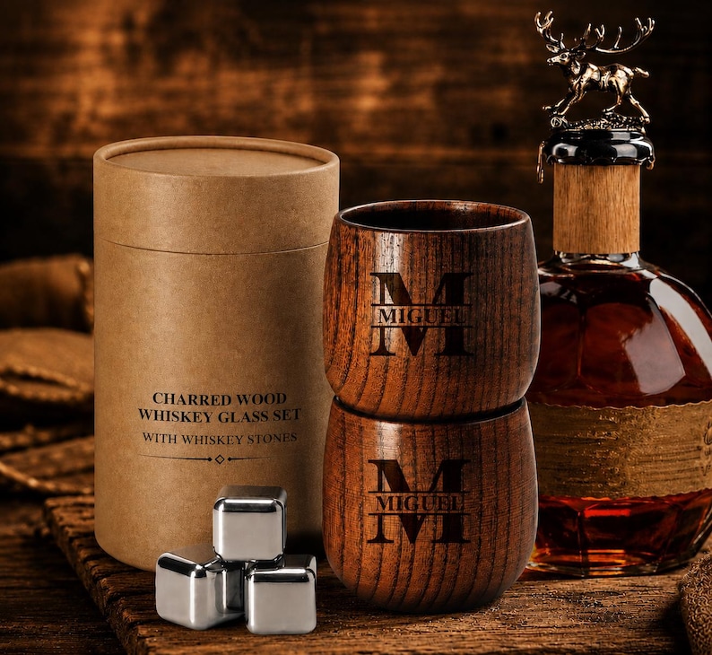 May include: A whiskey glass set with two wooden glasses engraved with "MIGUEL" and the letter "M". The set includes a bottle with a deer-shaped stopper, whiskey stones, and a cylindrical box that reads "CHARRED WOOD WHISKEY GLASS SET WITH WHISKEY STONES."