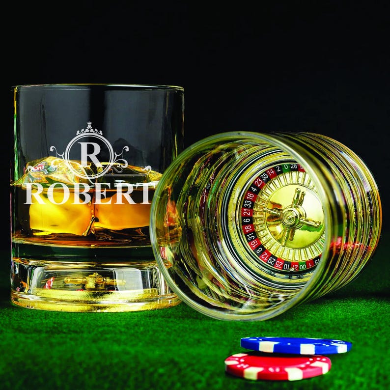May include: Two personalized whiskey glasses with gold rims. One glass has a roulette wheel design and the other has the name "ROBERT" engraved on it.
