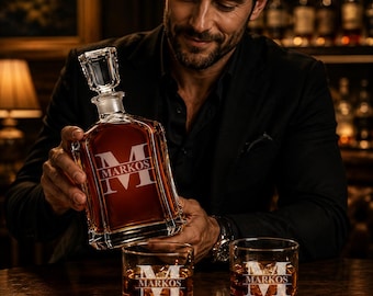 Puede incluir: Un decantador de whisky de cristal y dos vasos a juego, cada uno grabado con el nombre "MARKOS" en blanco. El decantador se está vertiendo en un vaso. Los vasos y el decantador están llenos de líquido ámbar. La escena está ambientada en un bar con poca luz.