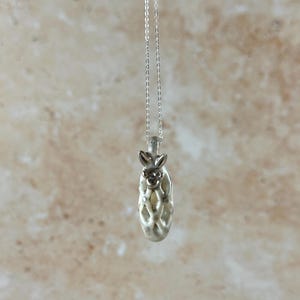 May include: A silver pendant necklace with a bunny design. The bunny sits atop an oval pendant with an openwork pattern. The chain is a delicate silver. The background has a light brown and beige marbled effect.