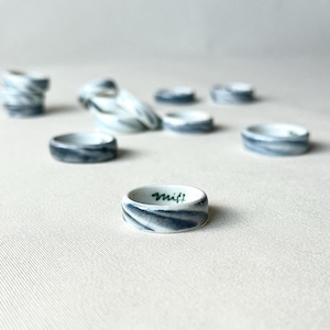 May include: A collection of ceramic rings with a marbled blue and white design. One ring in the foreground has the word "misfit" written in green. The rings are arranged on a neutral surface.