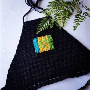May include: Black crochet halter top with a colorful square design in the center. The top has adjustable straps and a fringed hem.
