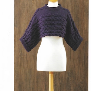 May include: A purple cropped sweater with a cable knit pattern. The sweater is displayed on a wooden mannequin.
