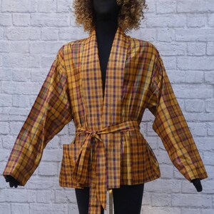 Peut inclure: Une robe en plaid jaune, violet et vert avec une ceinture à nouer. La robe a une silhouette longue et fluide et une coupe ample.