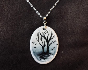 May include: A silver chain necklace with a white oval pendant featuring a black silhouette of two trees with bare branches and birds flying overhead.