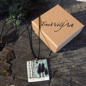 May include: Square pendant necklace with a black cord. The pendant features a hand-painted landscape with birch and evergreen trees, and birds. A brown box with the text "TreeWolfArt" is in the background.