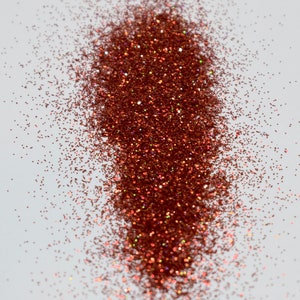 May include: A close-up of a pile of copper glitter on a white background. The glitter is iridescent and has a metallic sheen.