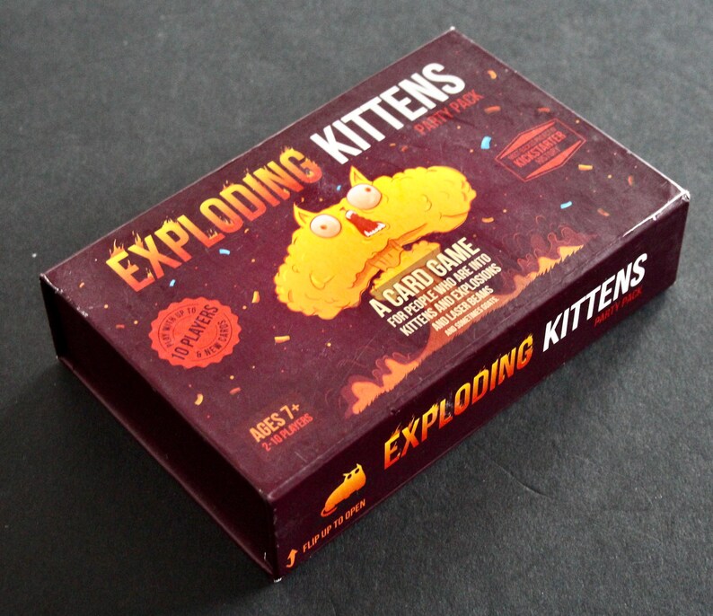 Peut inclure: Bo&icirc;te rectangulaire rouge fonc&eacute; pour le jeu de cartes "Exploding Kittens Party Pack". La bo&icirc;te pr&eacute;sente le titre du jeu en orange et blanc, et une image de chat jaune. Le texte comprend "Ages 7+" et "10 joueurs".