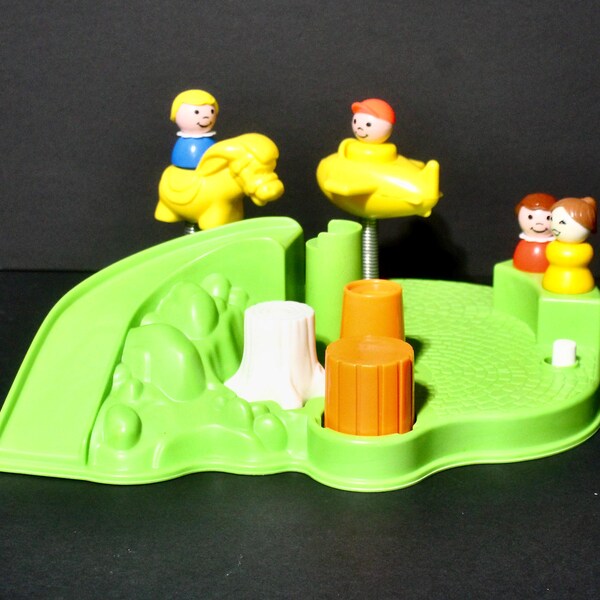 May include: A vintage children's toy with a bright green base, featuring a slide, trees, and figures riding a yellow elephant and a yellow submarine. The toy includes a small lever and several colorful figures.