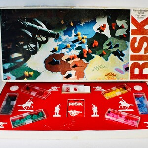 May include: Vintage Risk board game, featuring a world map with territories and miniature army pieces in various colors. The game box is open, revealing the game board and components. The box has the word "RISK" in large red letters.