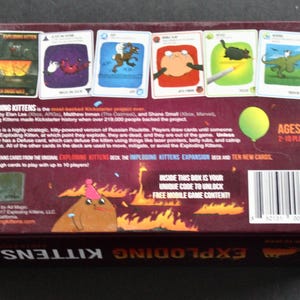 Peut inclure: Dos d'une bo&icirc;te de jeu de cartes Exploding Kittens marron. La bo&icirc;te pr&eacute;sente des illustrations de chats et d'autres personnages sur des cartes. Le texte comprend les d&eacute;tails du jeu, la tranche d'&acirc;ge et la phrase "&Agrave; L'INT&Eacute;RIEUR DE CETTE BO&Icirc;TE SE TROUVE VOTRE CODE UNIQUE POUR D&Eacute;BLOQUER DU CONTENU DE JEU MOBILE GRATUIT !"