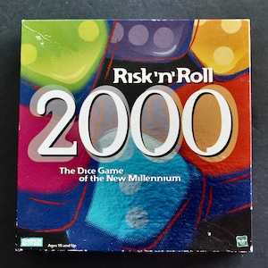 May include: A boxed board game titled "Risk 'n' Roll 2000." The box features large white numbers "2000" over a colorful dice-themed background. Text reads "The Dice Game of the New Millennium" and "Ages 10 and Up."