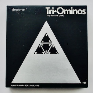 May include: A black and white Tri-Ominos game box. The box features a large white triangle with smaller black triangles inside, each with numbers. The game is for ages 8 to adult and for 2 to 6 players. The brand name "Pressman" is visible.