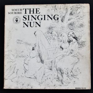 May include: Vintage album cover for "The Singing Nun" featuring a black and white illustration. The artwork depicts a nun playing a guitar, surrounded by other women and birds. The album title and artist's name are printed at the top.