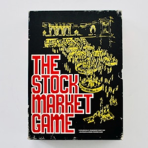 May include: A black box with a yellow and white illustration of a stock market scene. The text "THE STOCK MARKET GAME" is in red letters on the box. The text "AVALON HILL'S TRADEMARK NAME FOR ITS STOCKS & BONDS TRADING GAME" is in yellow letters on the bottom of the box.