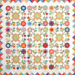 May include: A white quilt with a floral pattern. The quilt features a repeating design of green vines with pink, yellow, blue, and orange flowers. The quilt is surrounded by a border of colourful triangles.