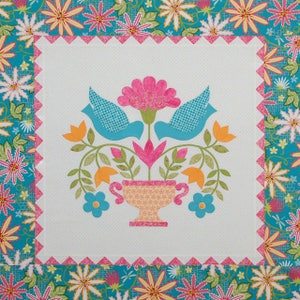 May include: A square quilt with a central design of a vase with flowers and two blue birds. The vase is yellow with a pink rim. The birds have a blue checkered pattern. The border is turquoise with floral patterns.