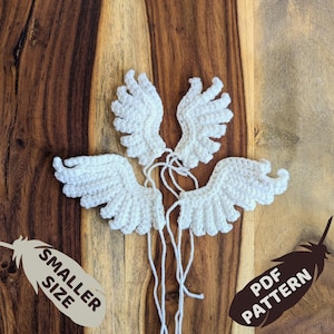 May include: Four white crocheted angel wings on a wooden surface. The wings are arranged in a cluster with the tips of the wings pointing outwards. The text "SMALLER SIZE" and "PDF PATTERN" are visible in the image.