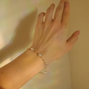 May include: A gold chain bracelet with clear crystal beads. The bracelet is on a person's wrist.