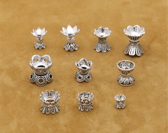 May include: Assortment of silver-toned metal bead caps with intricate designs. The caps are in various sizes and shapes, featuring floral and geometric patterns.