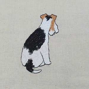 May include: Embroidered image of a white and black wirehaired fox terrier sitting with its tail curled. The dog is facing away from the viewer.
