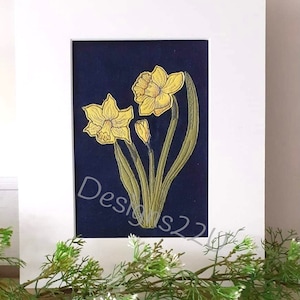 May include: A framed embroidery of three yellow daffodils with green stems and leaves on a dark blue background.