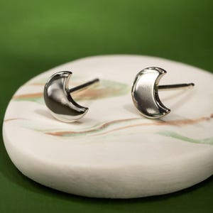 Könnte beinhalten: Ein Paar silberne Halbmond-Ohrstecker. Die Ohrringe sind klein und zart und perfekt für den Alltag.