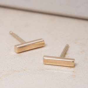 Peut inclure: Une paire de boucles d'oreilles en forme de barre en or. Les boucles d'oreilles sont simples et minimalistes, avec une forme de barre rectangulaire.