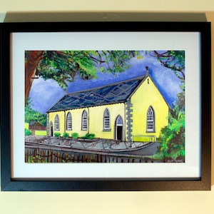Pode incluir: Pintura emoldurada de uma igreja amarela com um telhado azul escuro e janelas arqueadas. A obra de arte é ambientada em um fundo de árvores verdes e um céu azul. A pintura está em uma moldura preta.