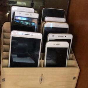 Pode incluir: Um organizador de madeira cheio de vários smartphones e tablets. Os dispositivos são uma mistura de branco e preto, com ecrãs visíveis. O organizador tem vários compartimentos e a madeira tem um acabamento claro e natural.