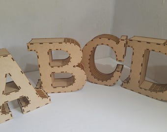 May include: Wooden letters A, B, C, and D, in a light brown color, are displayed. The letters are three-dimensional and have a layered construction with visible seams. The letters are on a white surface.