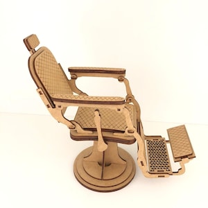 May include: A miniature wooden barber chair with a detailed design. The chair features a headrest, armrests, and a footrest. The seat and backrest have a diamond pattern. The chair is made of light brown wood and has a round base.