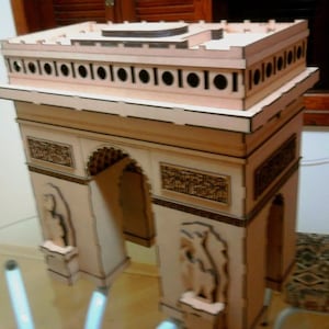 Pode incluir: Um modelo de madeira do Arco do Triunfo, com detalhes cortados a laser. O modelo é feito de madeira clara, mostrando o design arquitetônico com precisão. O arco inclui esculturas detalhadas e uma base retangular.