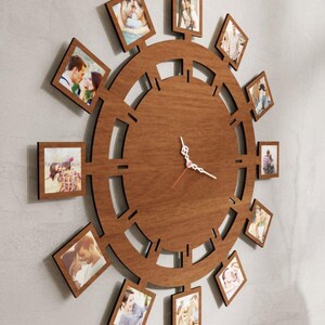 Pode incluir: Um relógio de parede circular de madeira castanha com um mostrador central, ponteiros brancos para as horas e minutos e um ponteiro dos segundos vermelho. A moldura é rodeada por doze molduras quadradas, cada uma com uma fotografia.