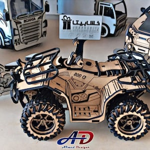 May include: A wooden model of an all-terrain vehicle (ATV) with the text "800 G" on the side. Other wooden vehicle models, such as a truck, motorcycle, and car, are also visible. The models are made of light brown wood with black detailing.