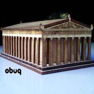 Op de afbeelding: Een houten model van een klassieke Griekse tempel, met een rechthoekige structuur en talrijke verticale zuilen. Het model is gemaakt van licht en donkerbruin hout, met ingewikkelde details op het dak en de gevel. Het woord "obuq" is links onderin zwart gedrukt.