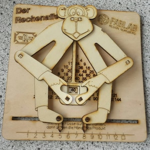 Op de afbeelding: Houten educatief speelgoed in de vorm van een aap met beweegbare ledematen en een getallentabel. De tekst "Der Rechenaffe" staat bovenaan, met "FABLAB REGION NÜRNBERG" en patentdata. De handen van de aap wijzen naar het getal 40.