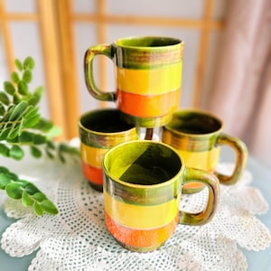 May include: Set of four green, yellow, and orange striped ceramic mugs. The mugs have a rustic, handmade look.