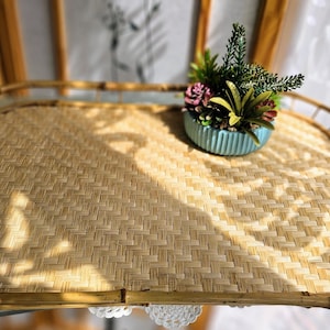 May include: A rectangular bamboo serving tray with a woven surface and curved edges. A small, light blue ceramic pot with a variety of succulents and greenery sits on the tray. The tray is on a glass surface.