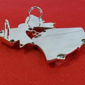 May include: Silver pendant in the shape of a stylized dancing figure. The pendant has a loop at the top for attaching to a chain.