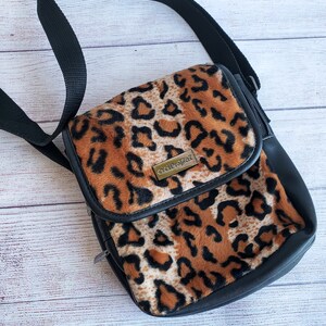 May include: A small black and brown leopard print crossbody bag with a black strap and a gold metal zipper pull. The bag has a gold metal logo that says "Sole Society".