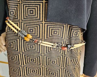 May include: A beaded belt with bone, amber, and red stone accents. The belt is worn over a black and gold patterned fabric.
